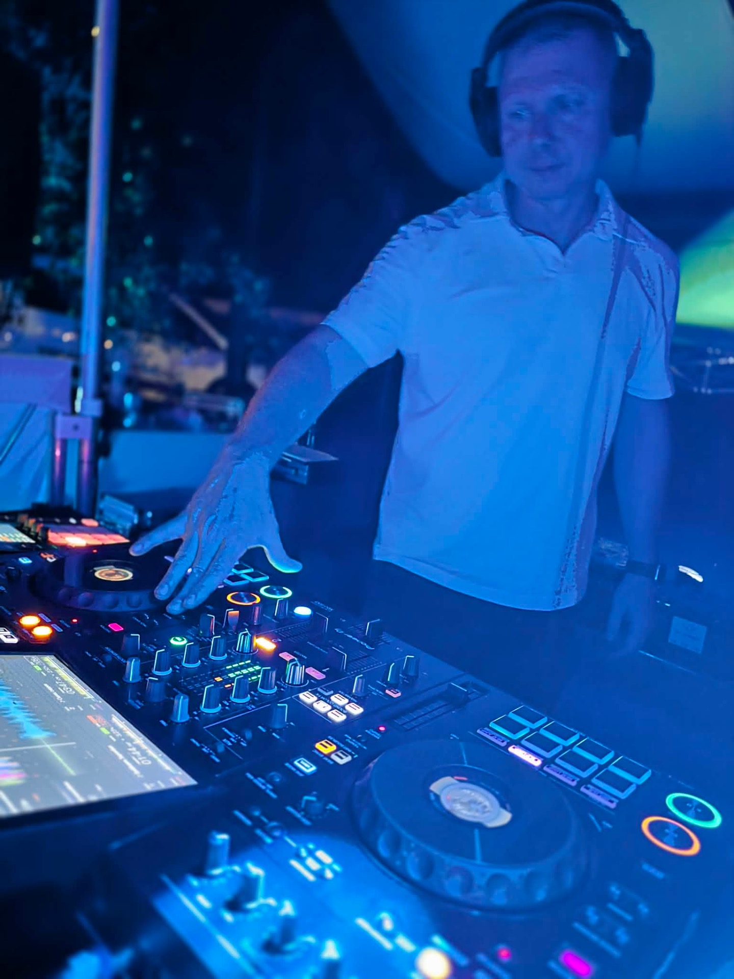 Kék fényben DJ férfi fejhallgatóval keverőpulton, gombok és csúszkák világítanak háttérben.